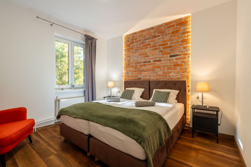 Izba 5 rodinného apartmánu 4+5 s posteľou a červeným kreslom